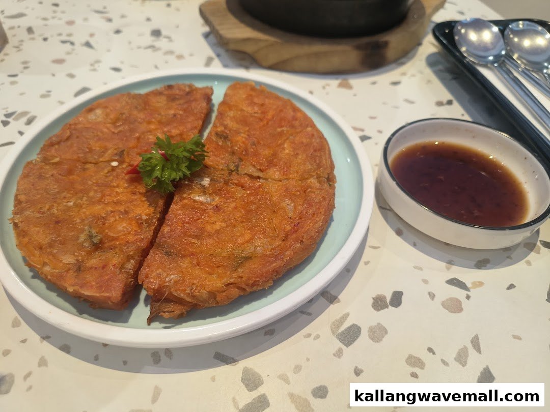 A vibrant Korean kimchi pancake served with a dipping sauce on a speckled table.