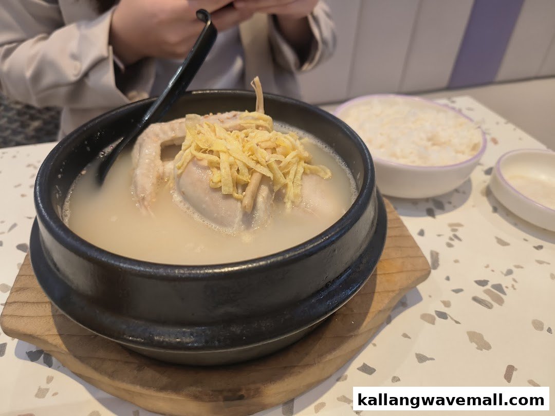 A hot pot of Samgyetang (Korean ginseng chicken soup) with rice on a table.