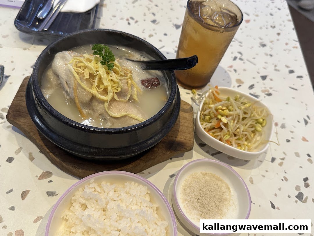 A steaming bowl of Korean ginseng chicken soup (Samgyetang) with rice and side dishes.
