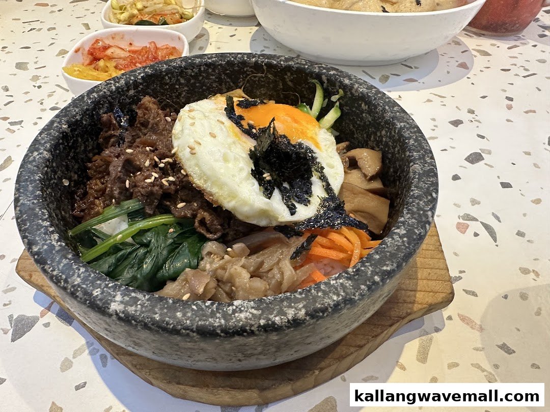 A vibrant Dolsot Bibimbap in a hot stone bowl, topped with a fried egg and various ingredients.