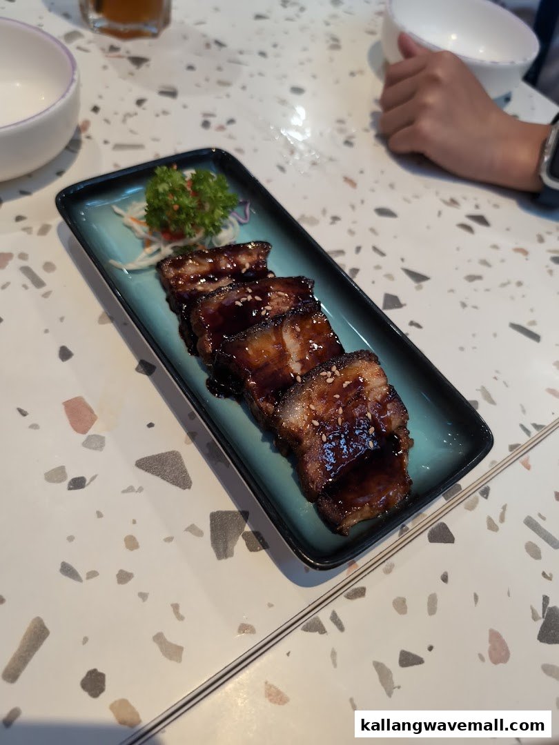 A plate of glazed meat slices with sesame seeds and a side garnish on a speckled table.