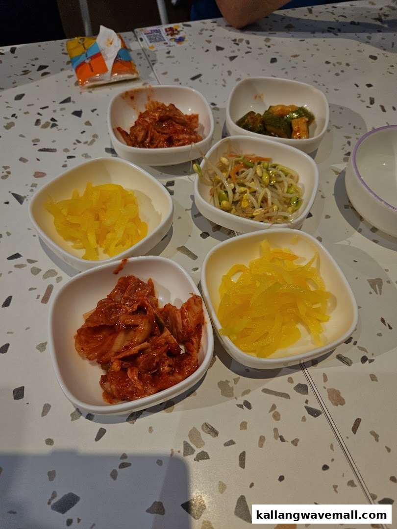 A table filled with various Korean banchan (side dishes) in white bowls.