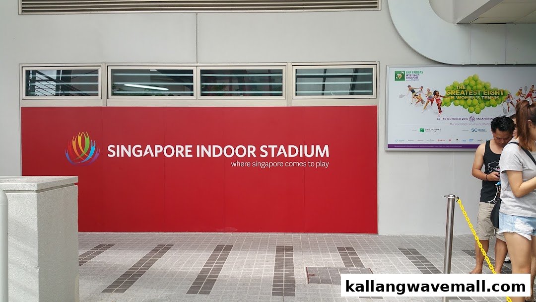 Exterior view of Singapore Indoor Stadium wall with event posters and people queuing.