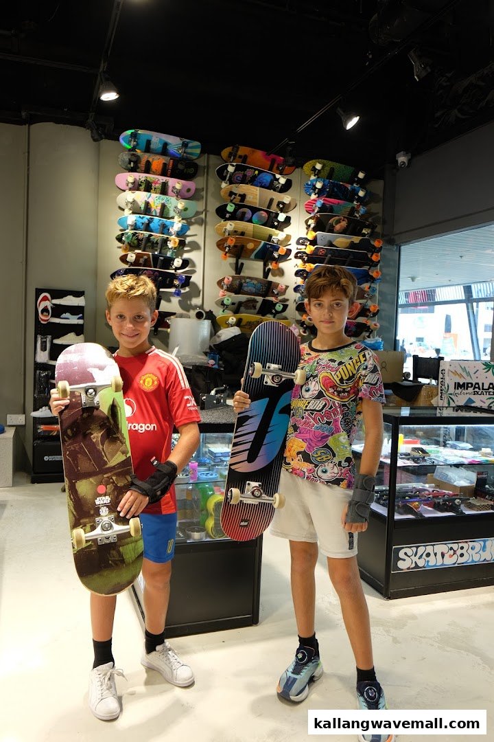 Two boys proudly display their skateboards inside Skatebruh Skate Shop, surrounded by a vibrant display of boards.