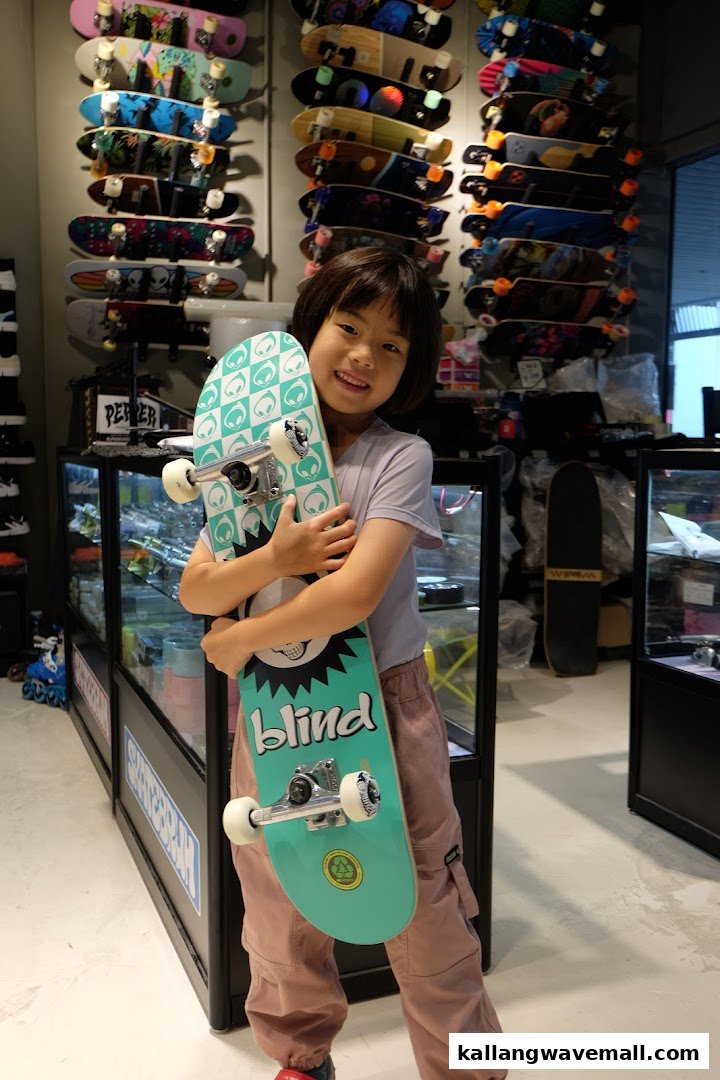A smiling child holds a new skateboard inside a vibrant skate shop filled with various boards.