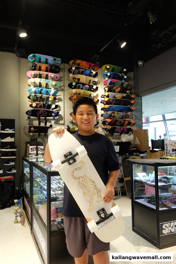 A smiling boy holds a new skateboard in a vibrant skate shop filled with various boards.