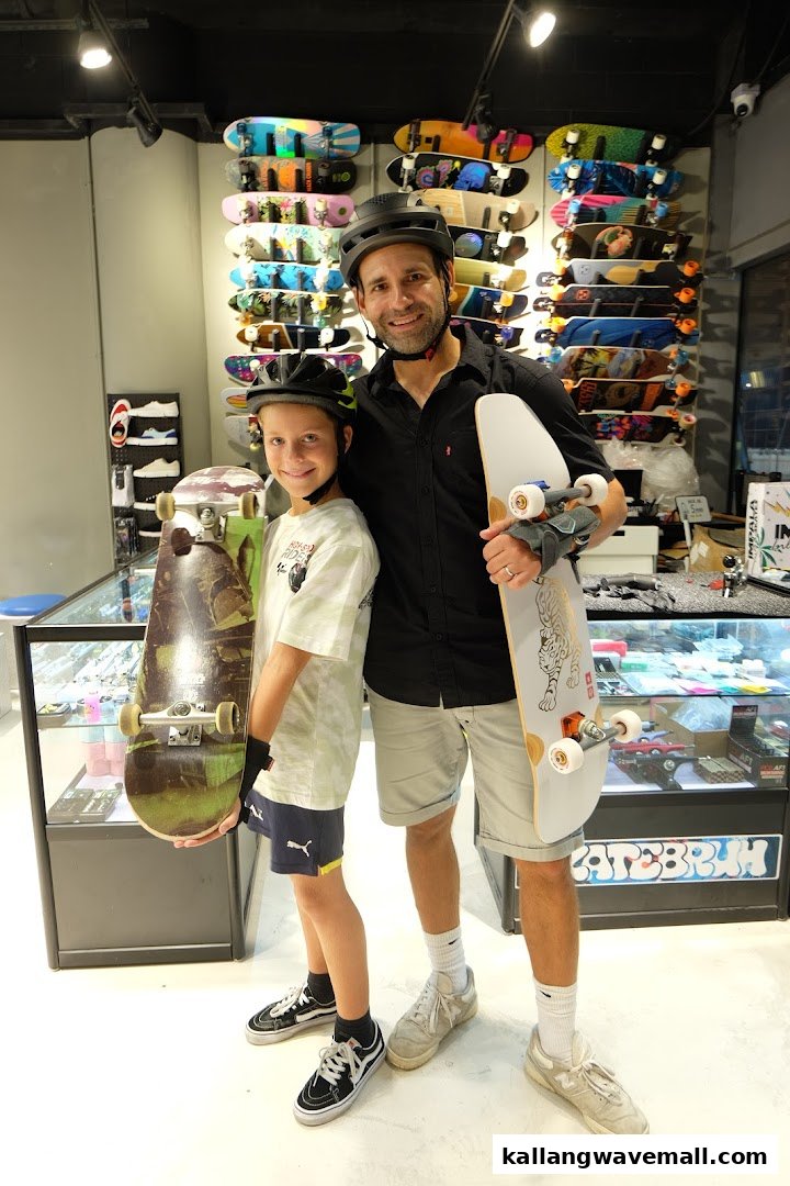 A man and a boy, both wearing helmets, pose with skateboards inside a vibrant skate shop.