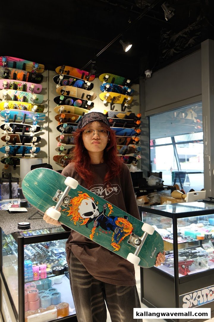 A person holds a skateboard with a flaming skull design inside a vibrant skate shop filled with various boards.