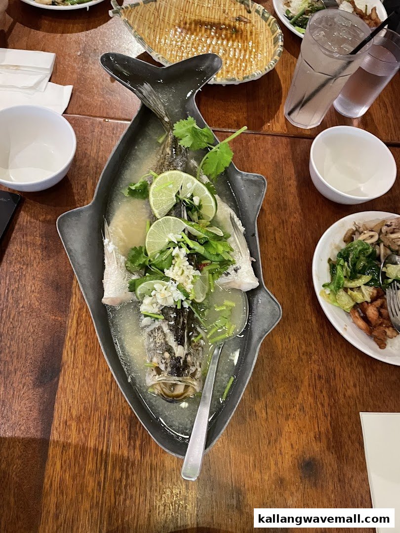 A steamed fish dish with lime and herbs on a fish-shaped platter, served on a wooden table.