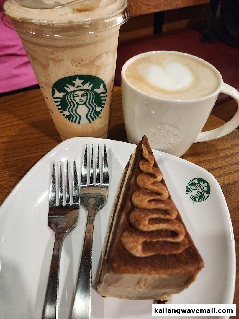 A Starbucks Frappuccino, latte with heart art, and a slice of cake on a white plate.