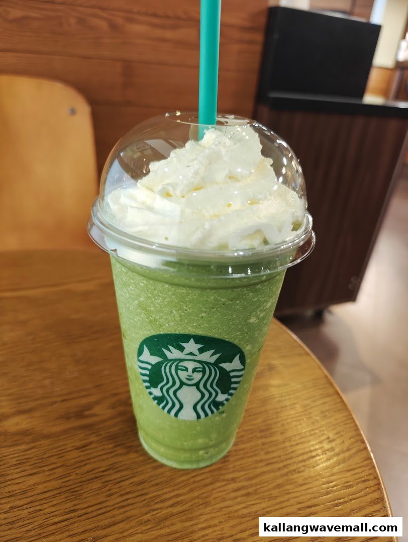 A vibrant green Starbucks Frappuccino topped with whipped cream and a straw on a wooden table.