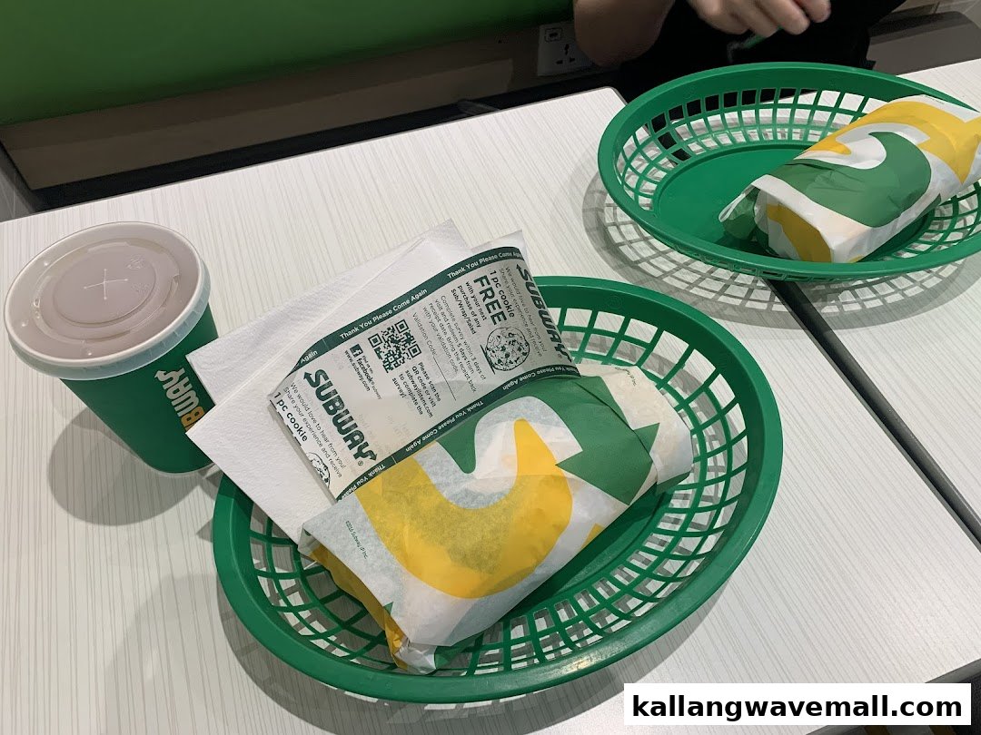 Two Subway meals with sandwiches and a drink served in green baskets on a white table.