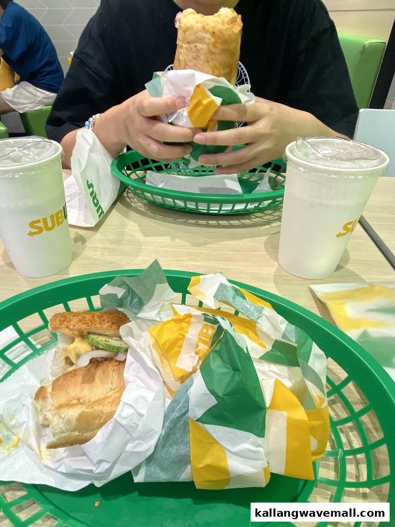 Customers enjoying fresh Subway sandwiches and drinks at a table.
