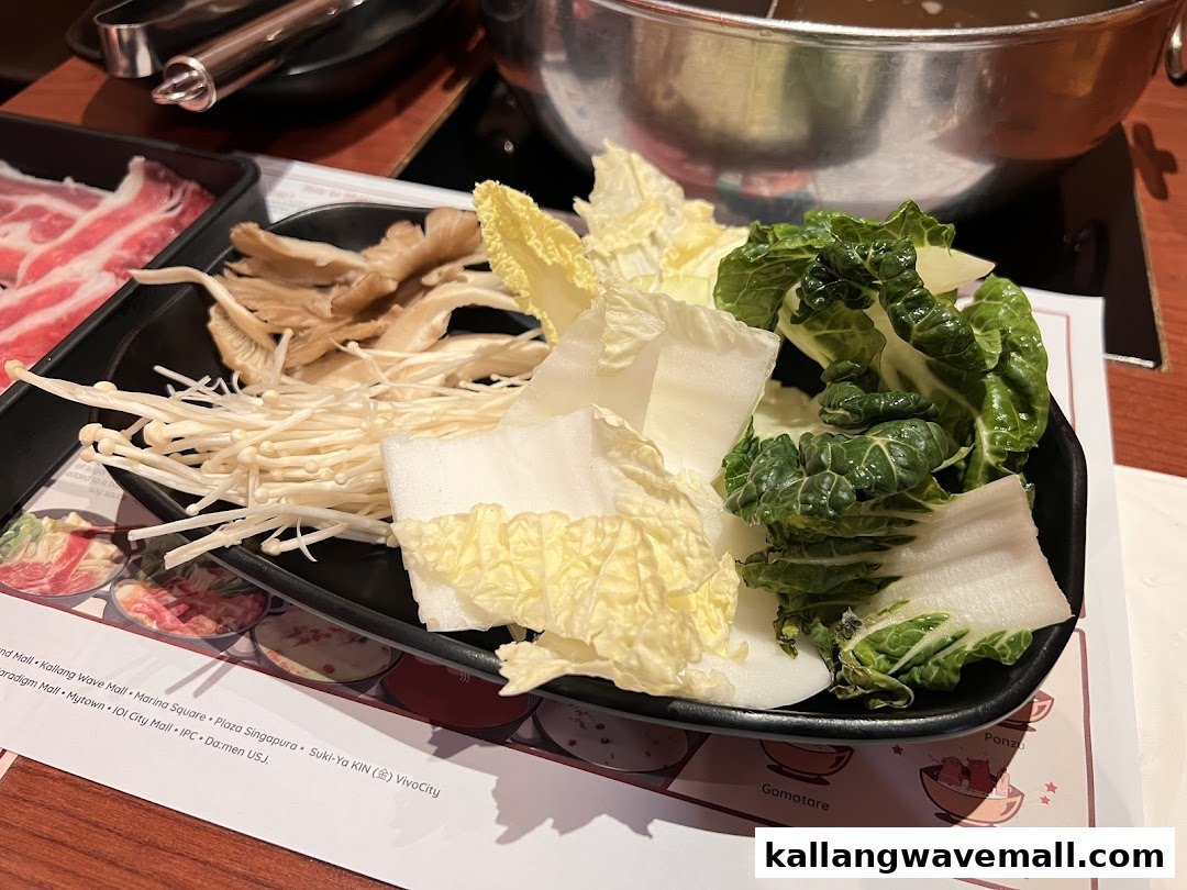 A vibrant platter of fresh vegetables and mushrooms alongside sliced meat, ready for a shabu-shabu hot pot.