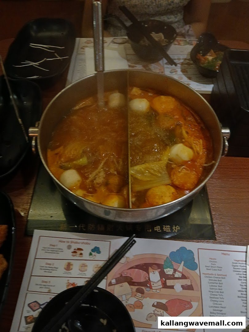 A bubbling shabu-shabu hot pot with two broths and ingredients on a dining table.
