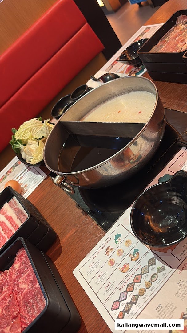 A close-up of a shabu-shabu hot pot with raw ingredients and a placemat menu on a wooden table.