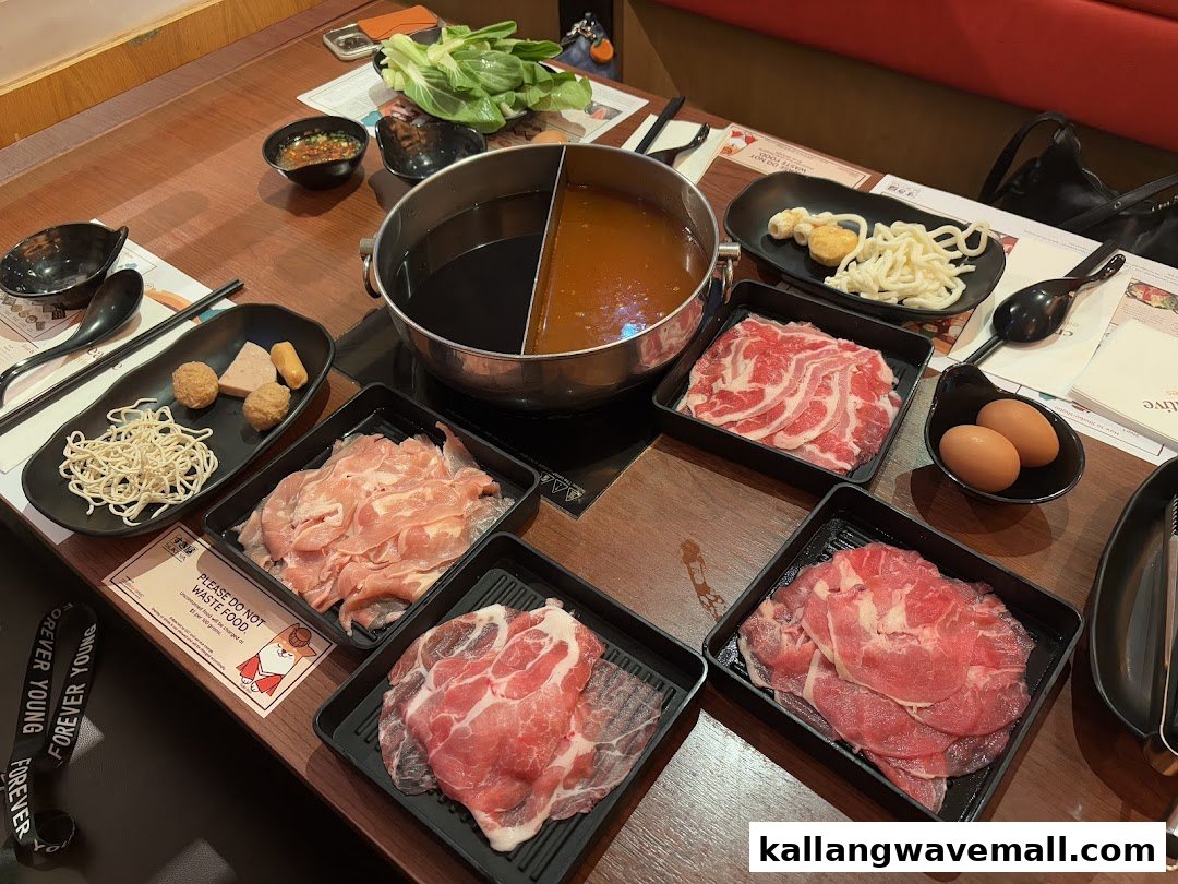 A table laden with a shabu-shabu hot pot, various raw meats, fresh vegetables, and noodles, ready for cooking.