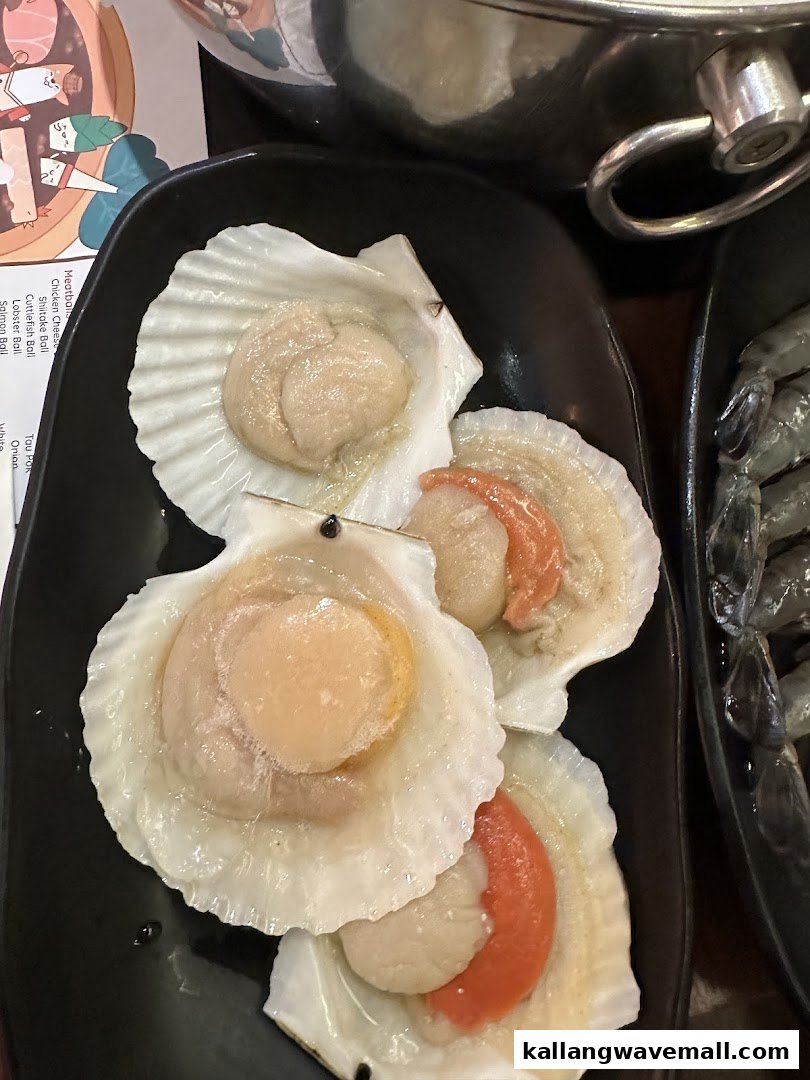 A close-up of fresh scallops in shells on a black plate, with a partial menu visible.