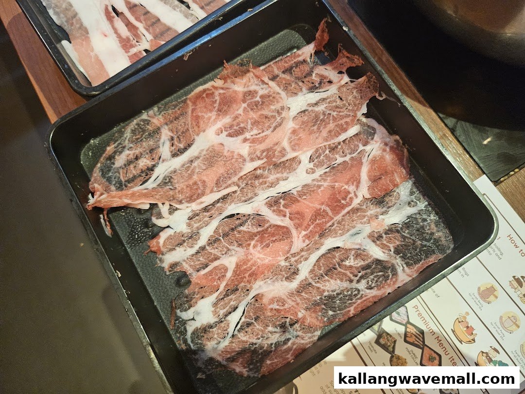 Close-up of thinly sliced marbled meat on a black tray, ready for shabu-shabu.