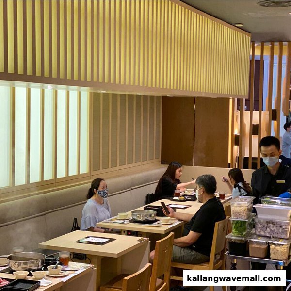 Diners enjoying shabu-shabu in a modern, well-lit restaurant interior with staff attending.