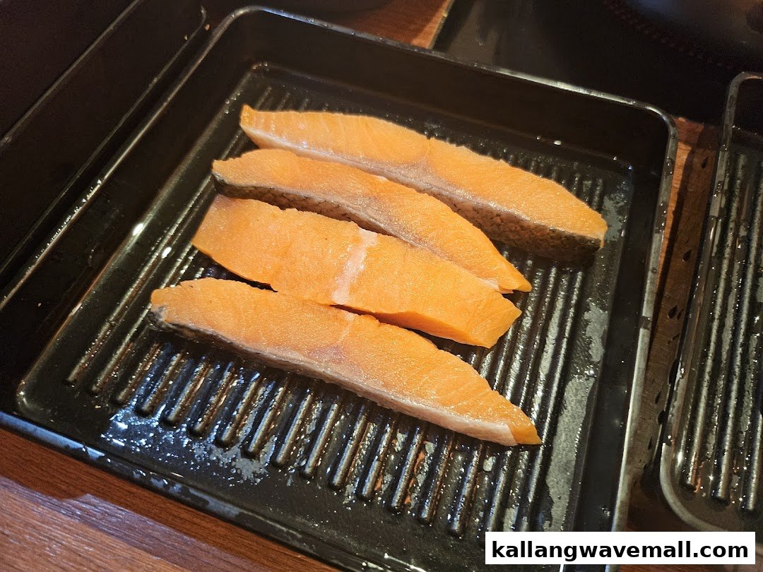 Four fresh salmon fillets are neatly arranged on a black ribbed tray, ready for shabu-shabu.