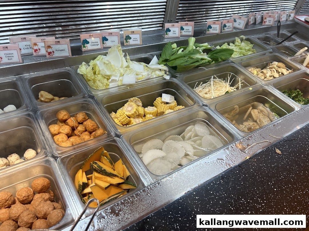 A self-serve buffet counter displaying various fresh ingredients for shabu-shabu, including vegetables and meat balls.