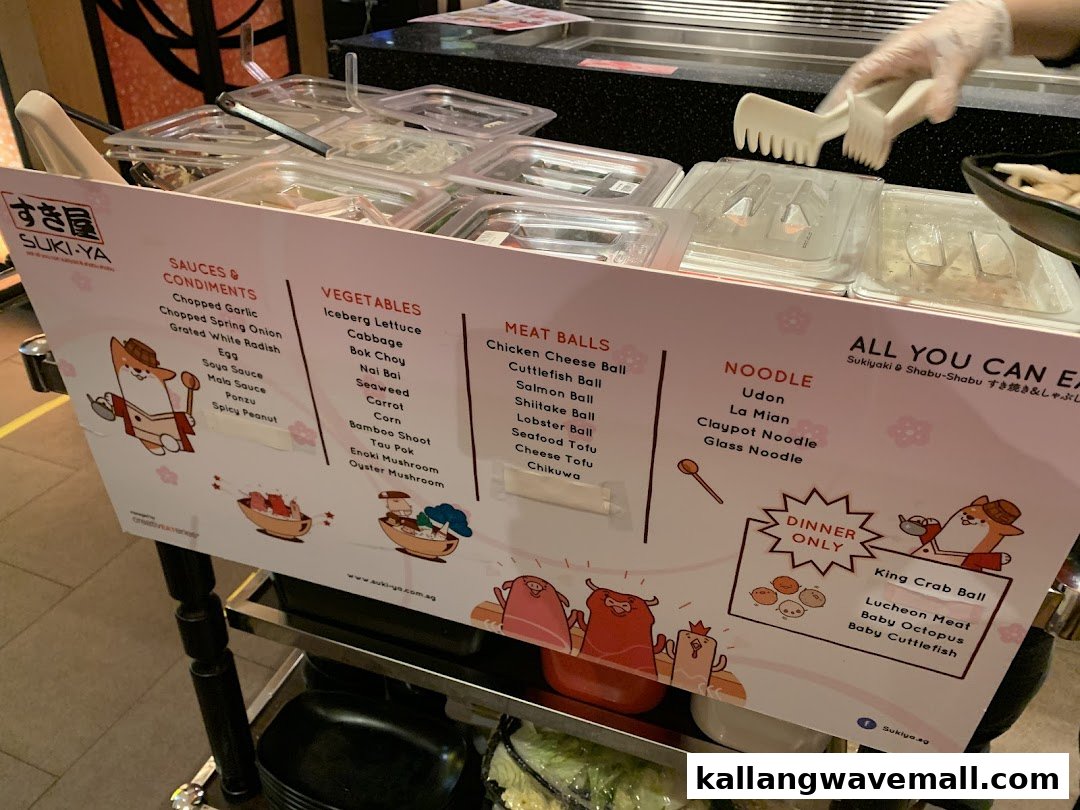 A self-serve counter displaying various shabu-shabu ingredients and a detailed menu board at Suki-Ya.