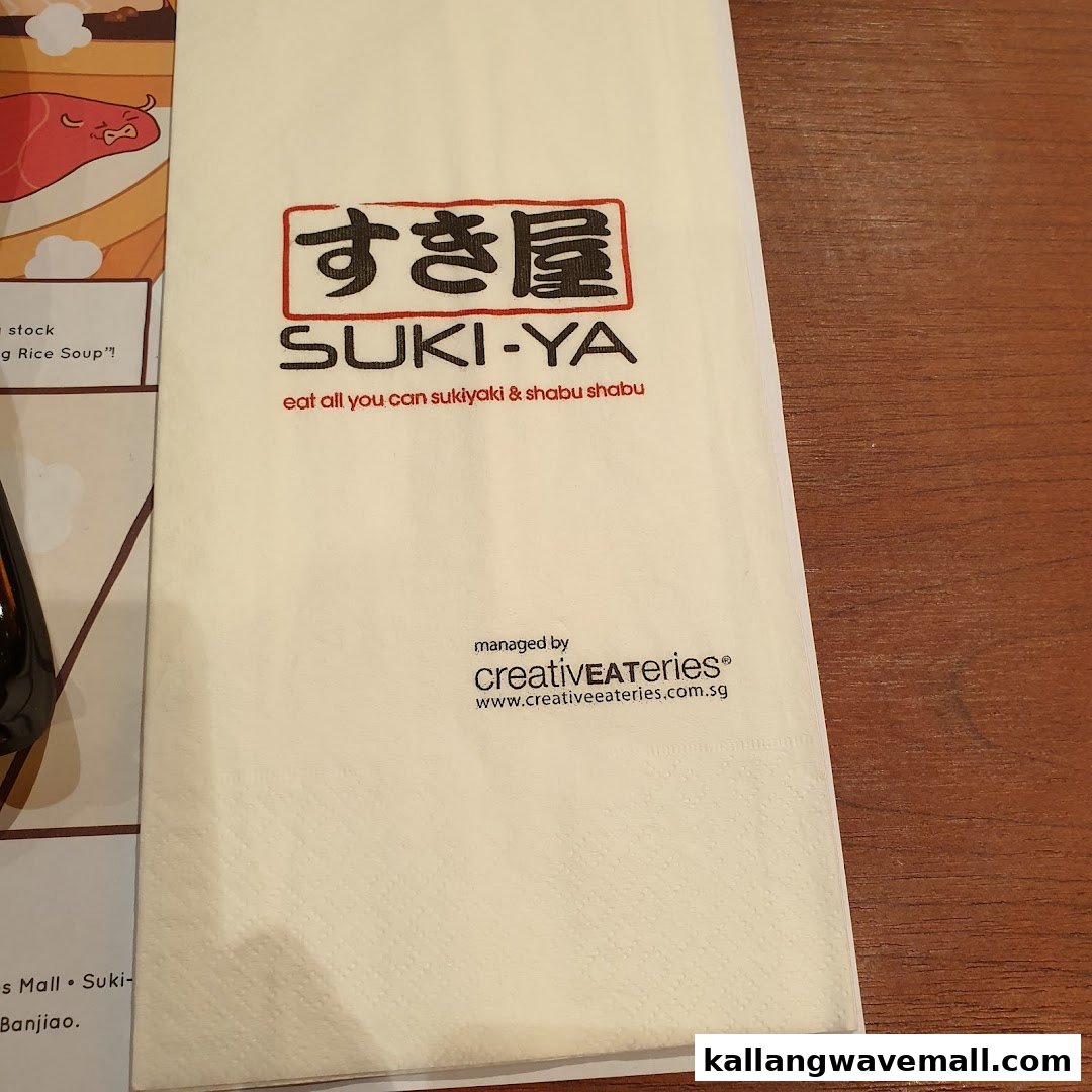 A Suki-Ya branded napkin/placemat displaying their logo and all-you-can-eat sukiyaki & shabu shabu slogan.