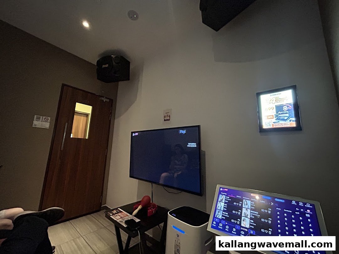 Interior of a modern KTV room with a large screen, touchscreen song selector, and speakers.