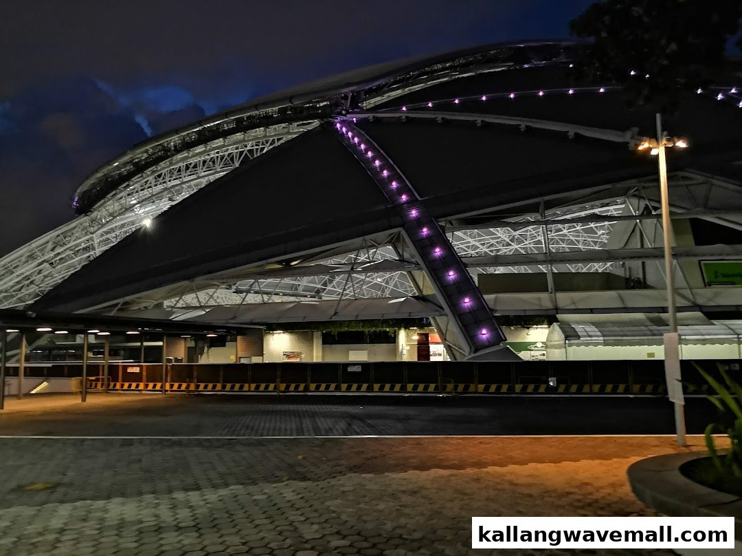 Night view of Kallang Wave Mall's impressive illuminated exterior, showcasing its modern architecture and vibrant purple lights.