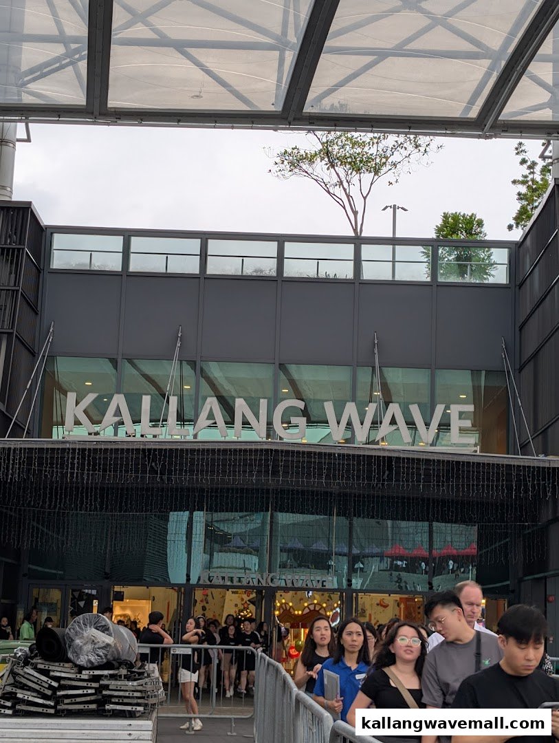Exterior view of Kallang Wave Mall entrance with people queuing under a modern glass canopy.