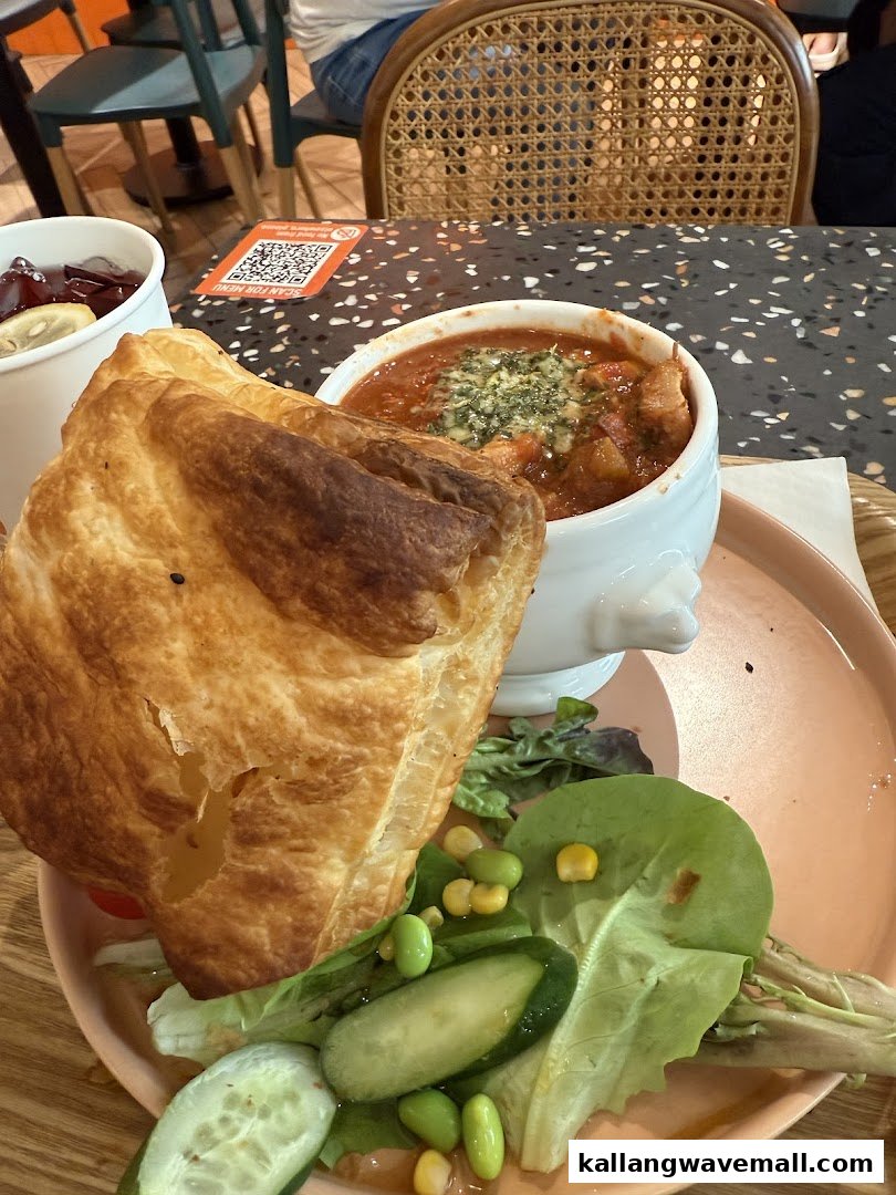 A hearty soup with a golden puff pastry top, fresh salad, and a drink on a table.