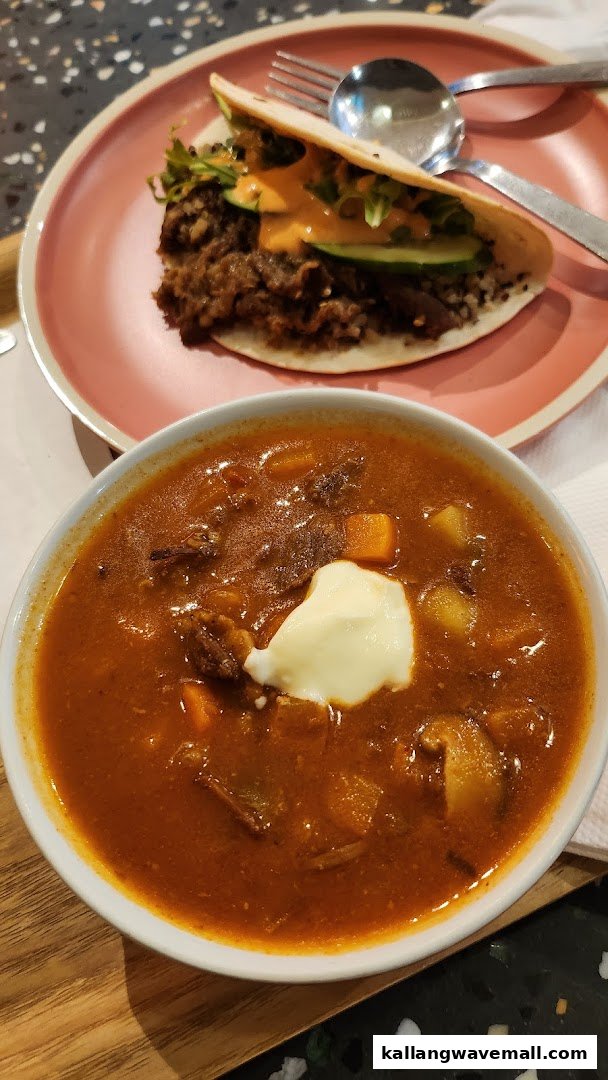 A hearty bowl of soup with a dollop of cream and a savory taco/wrap on a plate.