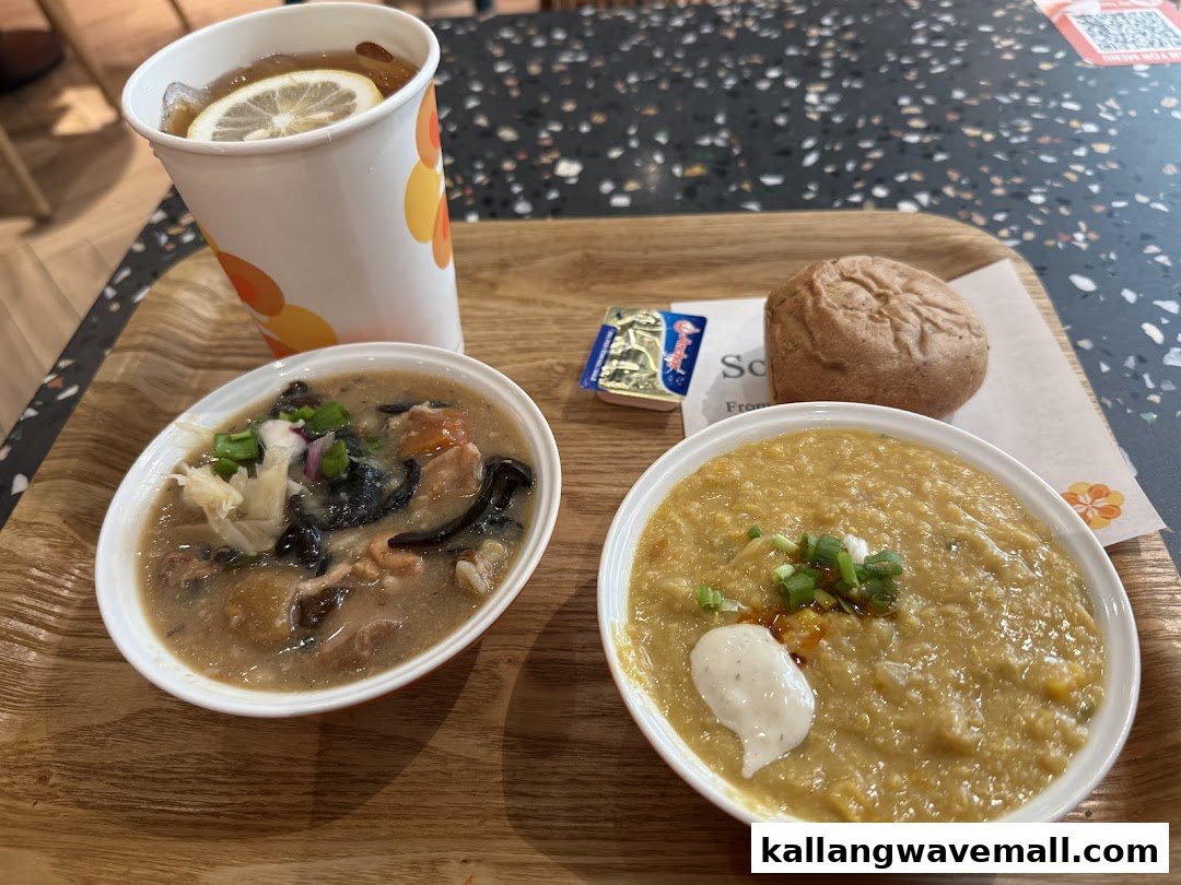 A meal tray featuring two bowls of soup, a bread roll, butter, and a lemon tea drink.