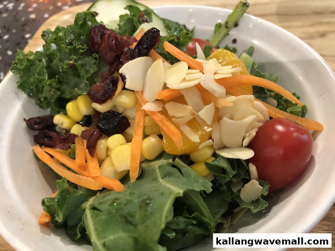 A vibrant bowl of fresh salad with kale, corn, carrots, tomato, dried fruit, and almonds.