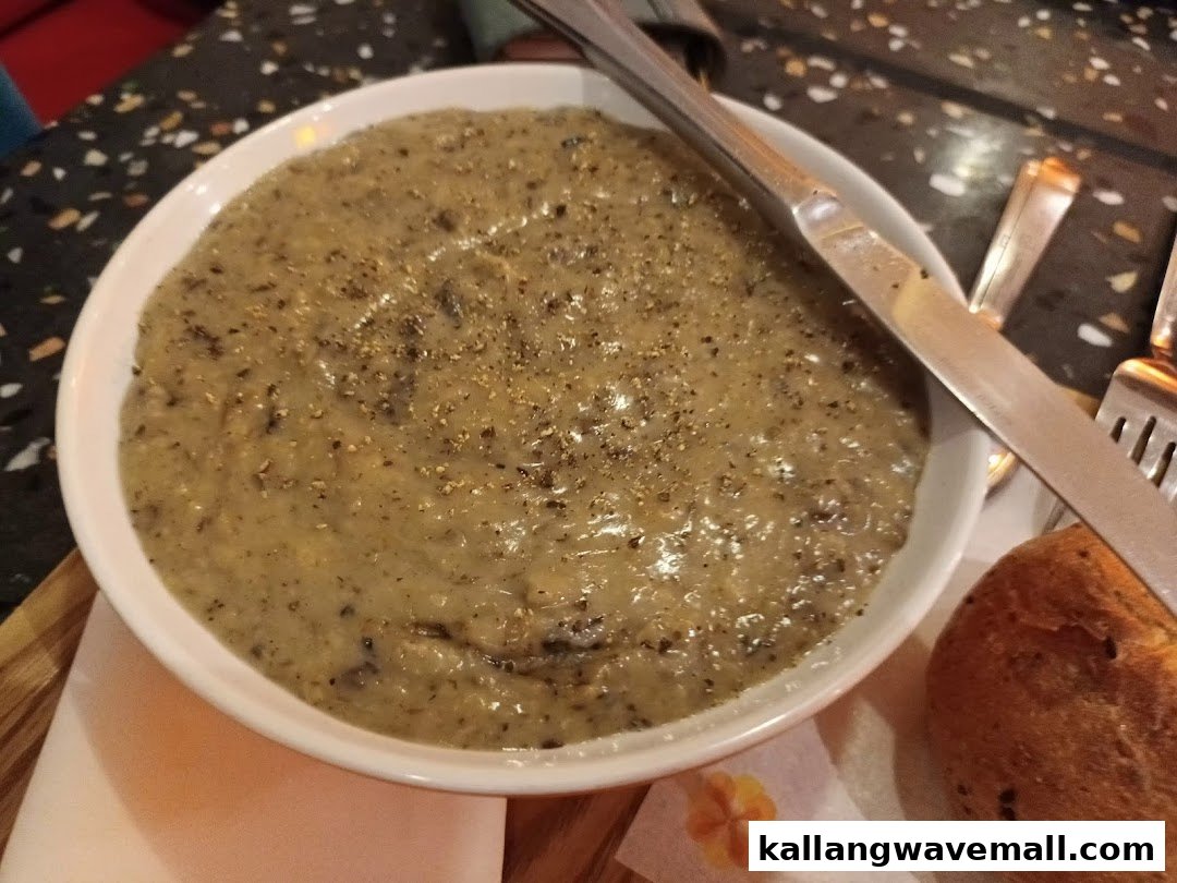 A close-up of a creamy mushroom soup in a white bowl, served with a side of bread.