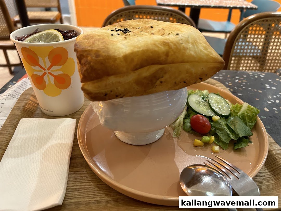 A hearty soup with a golden pastry crust, fresh side salad, and a refreshing drink on a tray.