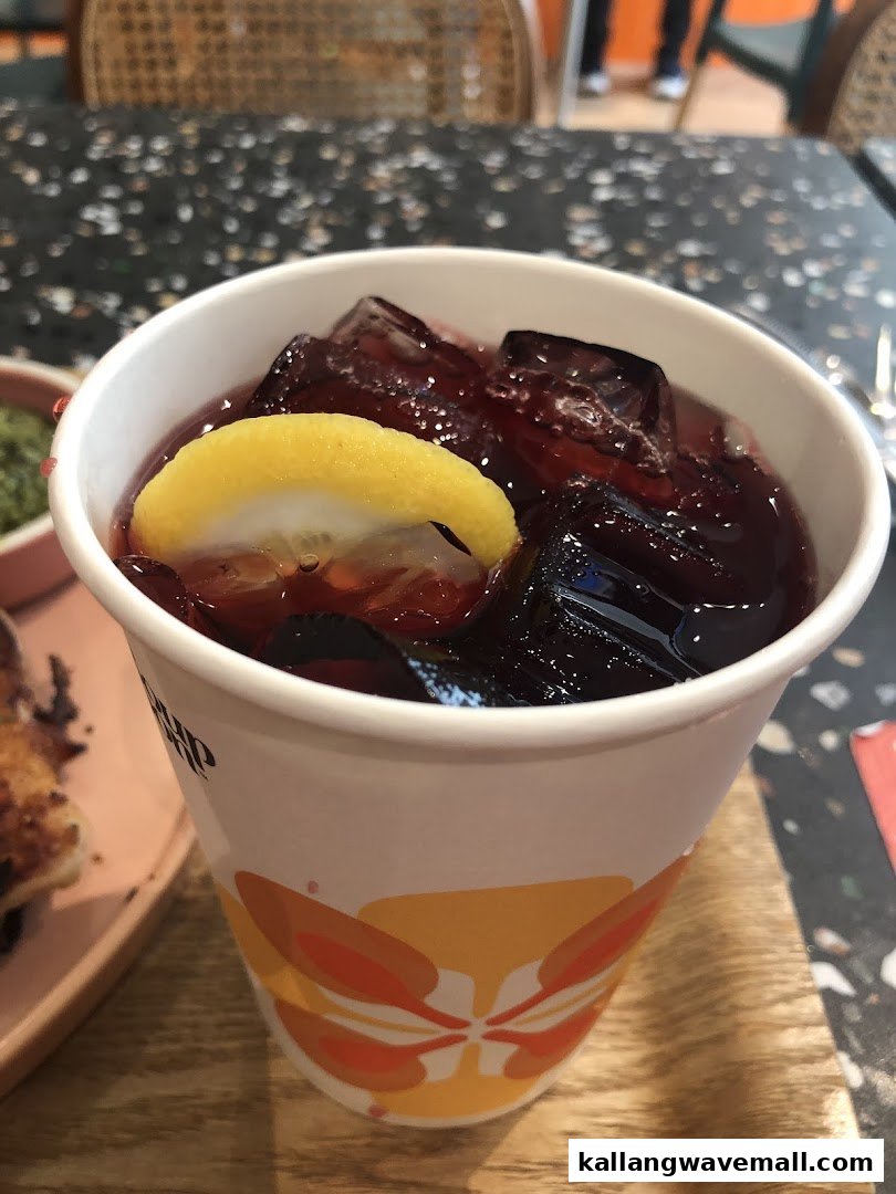 A refreshing berry-colored drink with ice and a lemon slice in a branded cup.