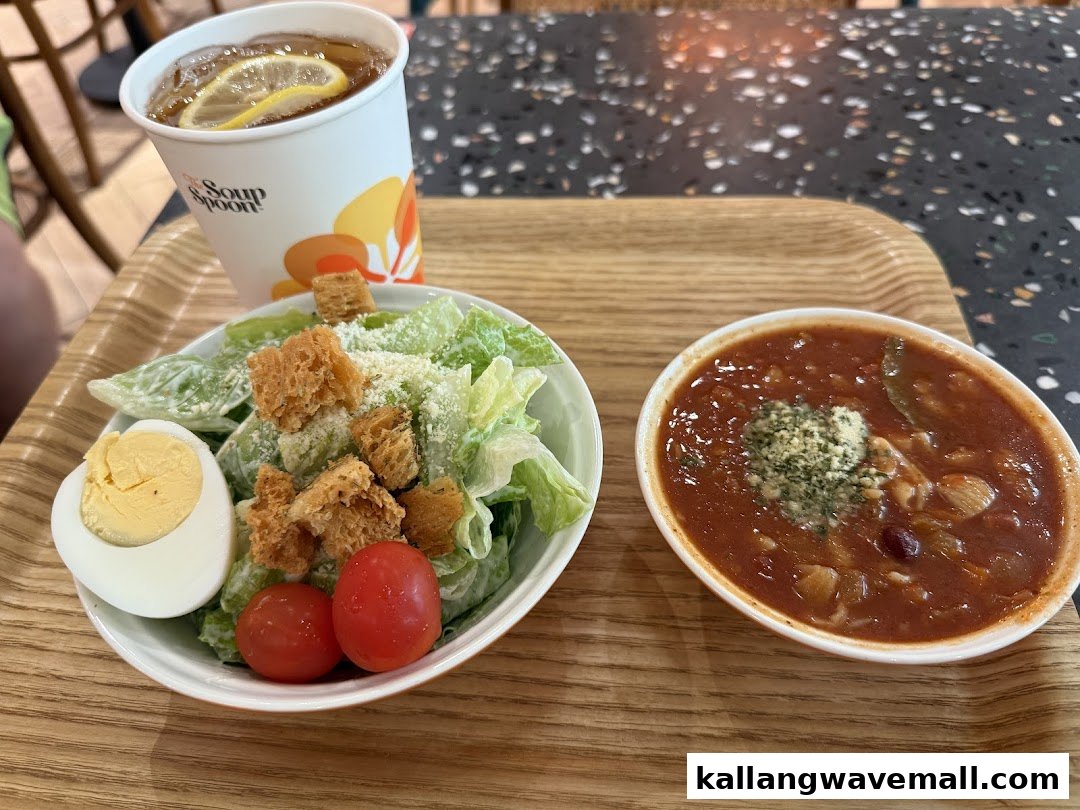 A hearty meal featuring a bowl of soup, a fresh Caesar salad, and iced lemon tea on a wooden tray.