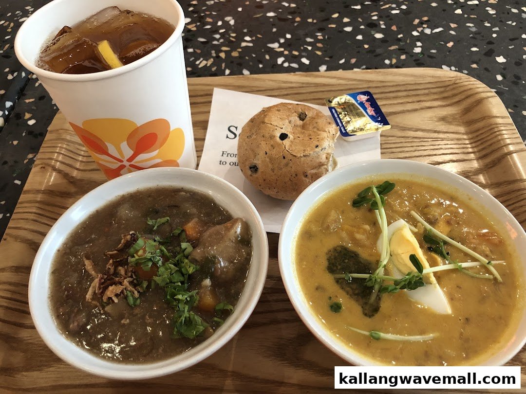 A tray featuring two bowls of hearty soup, a bread roll with butter, and a refreshing iced tea.