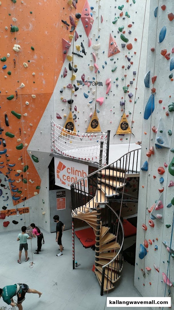 An indoor climbing gym featuring colorful walls, a spiral staircase, and climbers preparing for activity.