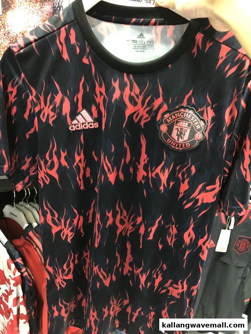 A black and red Manchester United football jersey by Adidas displayed in a retail store.