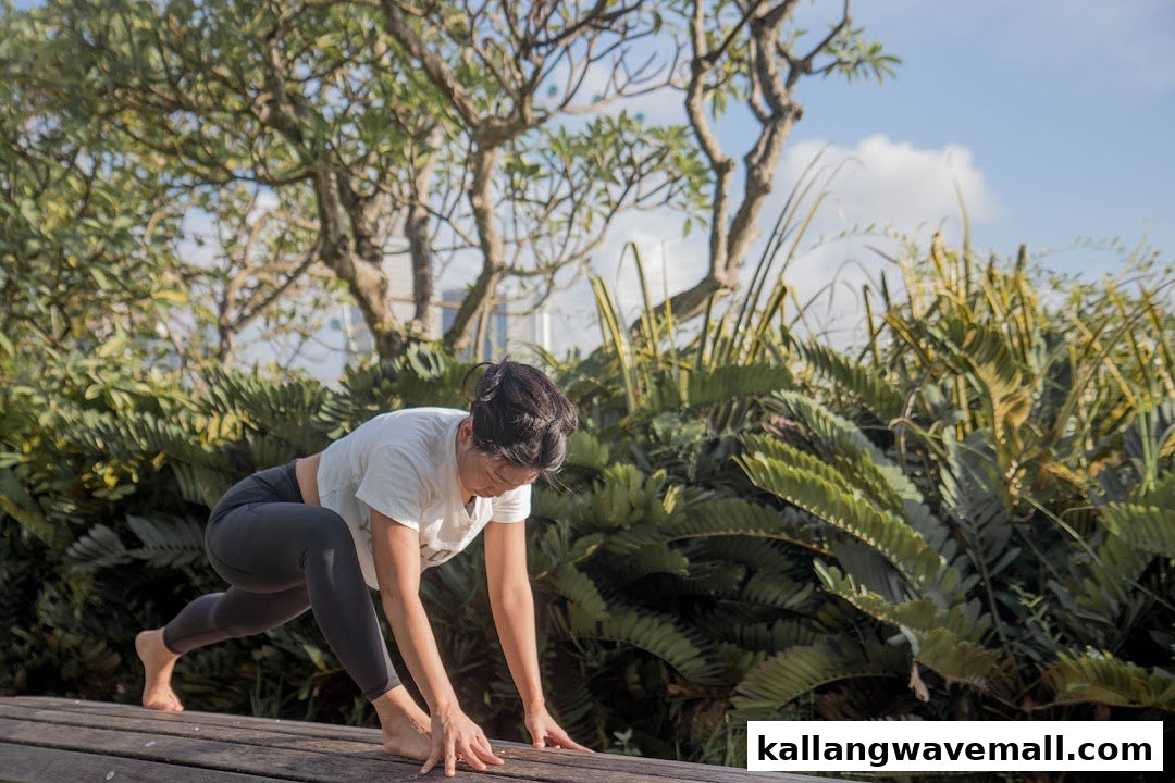 A person in yoga attire performs a lunge pose outdoors on a wooden deck amidst lush greenery.
