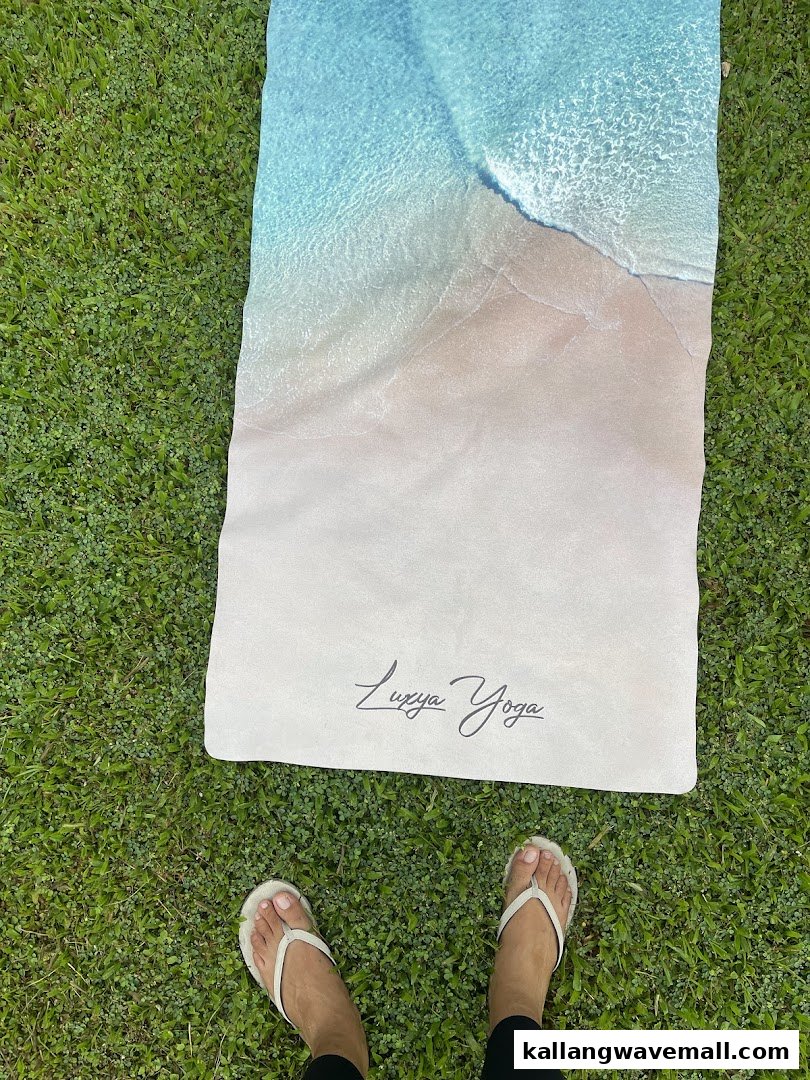 A person's feet on a yoga mat featuring a beach design, set on green grass.