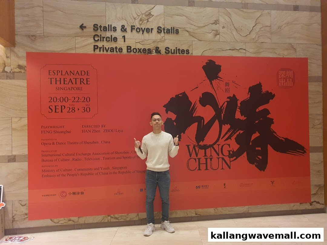 A person poses in front of a large red banner advertising the 'Wing Chun' performance at Esplanade Theatre.