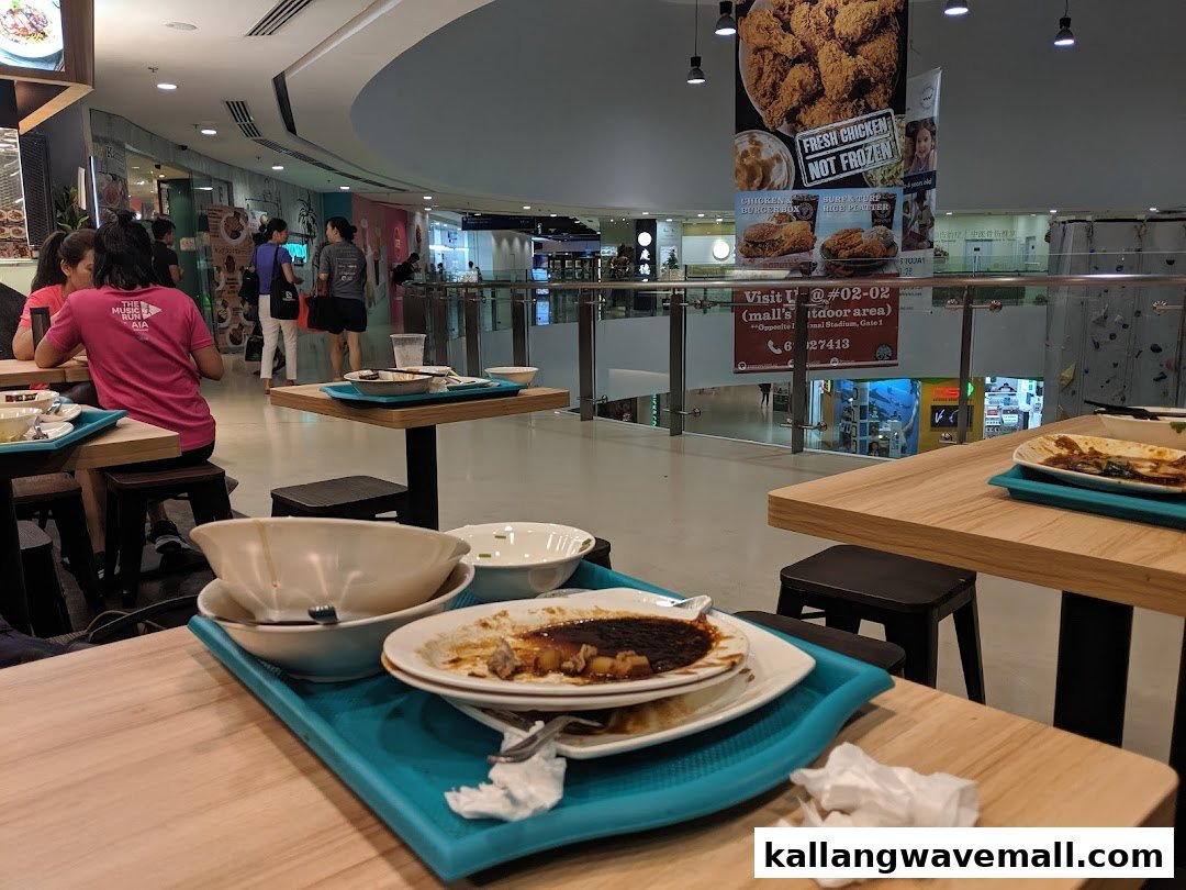 A bustling food court dining area with tables, chairs, and patrons enjoying their meals.
