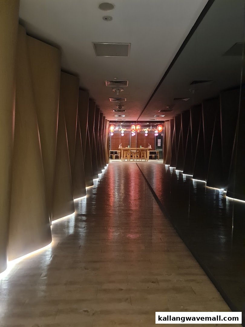 A long, dimly lit hallway with textured walls leads to a bright seating area with red lanterns.