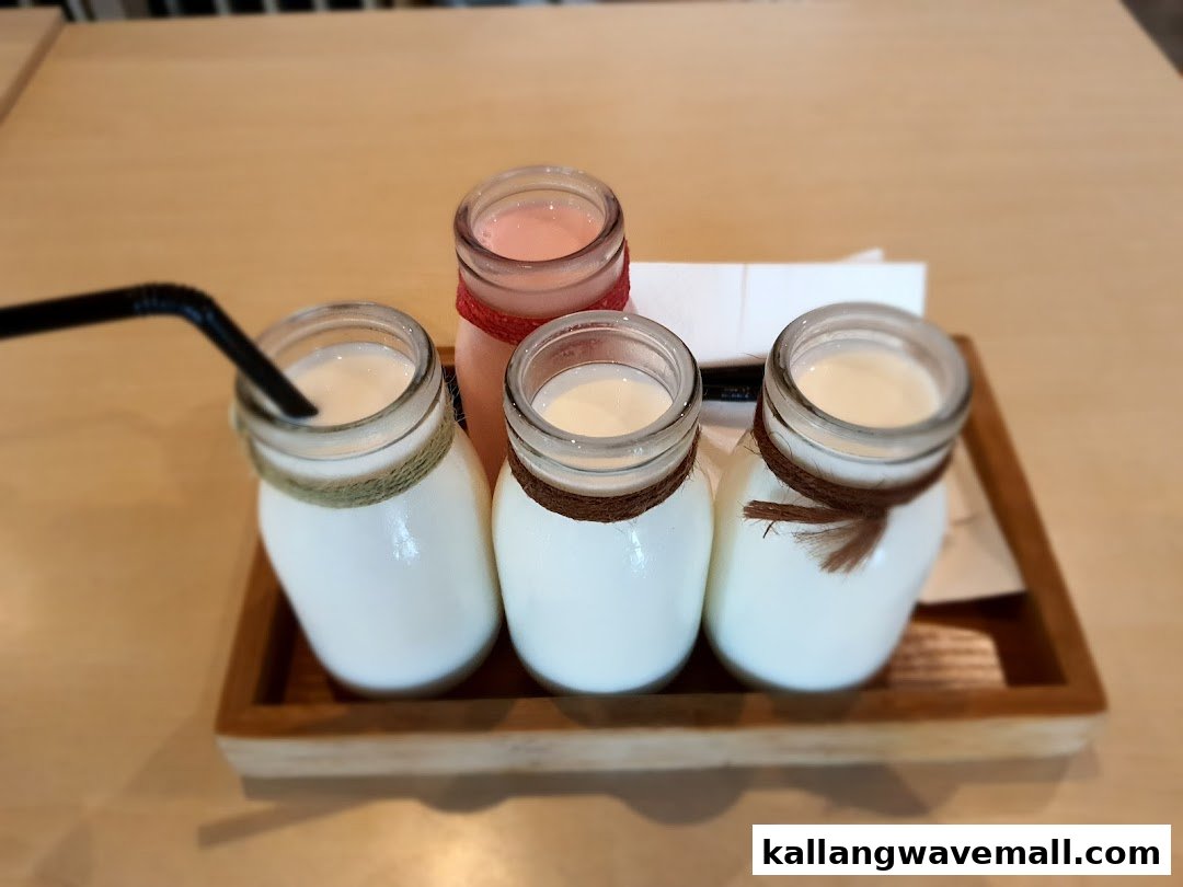 Four small bottles of refreshing drinks, including milk and a pink beverage, served on a wooden tray.