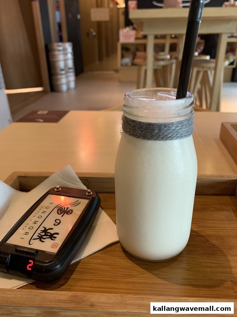 A refreshing drink in a glass bottle with a straw and a service pager on a wooden tray.