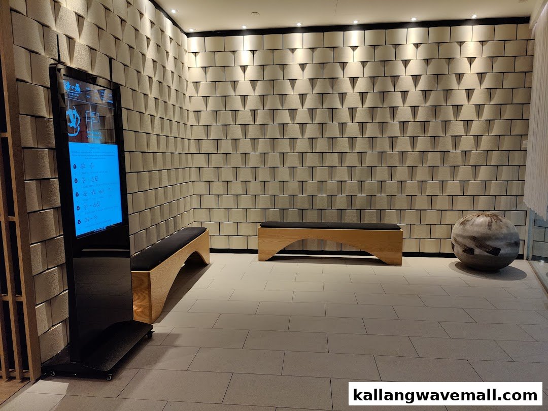 A modern spa waiting area featuring textured walls, wooden benches, and a digital information screen.
